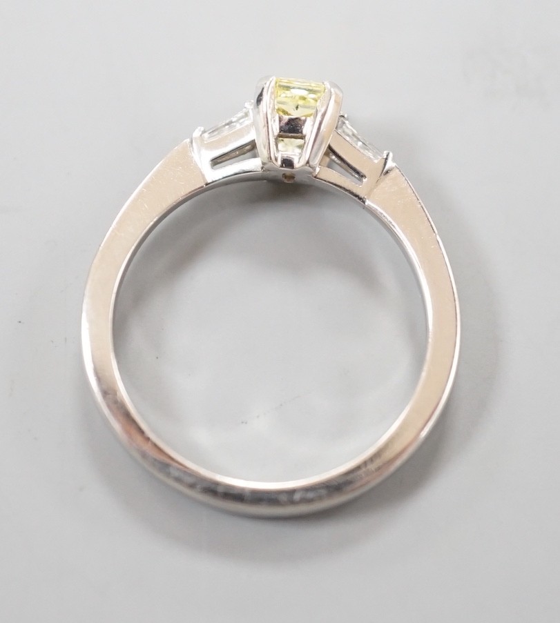 A modern platinum and single stone fancy yellow diamond set ring, with trapeze cut diamond set shoulders, size N, gross weight 4.6 grams